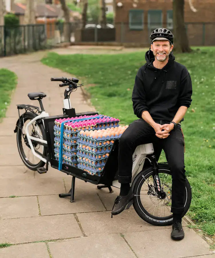 Man sitting on a cargo bike loaded with egg crates.